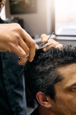 Bir kuaför, çağdaş bir berber dükkanında müşterisinin saçını keserken dikkatle odaklanır. Doğal ışık pencereden akar ve öğleden sonra sıcak bir atmosfer yaratır..