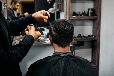 Şık bir berber dükkanında, yetenekli bir kuaför, oturan bir müşterisine titiz bir saç kesimi yapmaya odaklanır. Atmosfer profesyonel ve misafirperver, yakınlarda çeşitli aletler var..