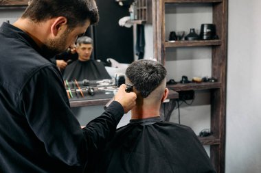 Yetenekli bir kuaför, iyi donanımlı bir berber dükkanında müşterisinin saçını dikkatlice kesiyor. Atmosfer profesyoneldir, kuaför aletleri ve saç kesimindeki detaylara dikkat çeker..