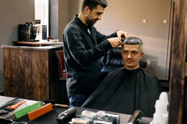 Bir kuaför modern bir berber dükkanında bir müşterinin saçını keserken ustalıkla makas yapar. Atmosfer canlı ve davetkar, gösterişli şık dekor ve aletler.