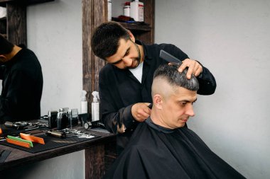 Yetenekli bir kuaför, iyi donanımlı bir berber dükkanındaki müşterisine yeni bir saç kesimi yapmak için özenle çalışır. Atmosfer canlı ve davetkar, tımar için mükemmel..
