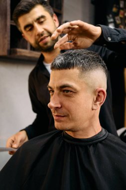 Yetenekli bir kuaför, çağdaş bir berber dükkanında müşterinin saçını titizlikle kesiyor..