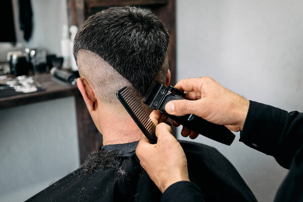 A skilled hairdresser expertly cuts a client's hair in a well-lit barbershop. The focus is on using a comb and trimmer for a clean, edgy style that showcases precision and care.