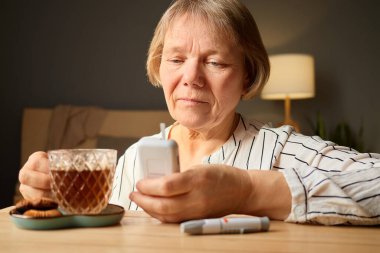 Son sınıf öğrencisi bir kadın ahşap bir masada oturup telefonunu kontrol ederken bardaktan çay yudumluyor. Kurabiyeler, sıcak ve davetkar bir odada, onun yanında küçük bir tabağa konur..