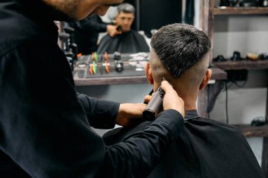 Yetenekli bir berber, çağdaş bir kuaförde müşterinin saçını dikkatlice keser. Parlak ışıklar modern dekoru aydınlatır çünkü araçlar yakınlarda düzgünce düzenlenmiştir..