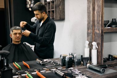 Bir berber şık bir salonda müşterinin saçını ustalıkla keser. İç kısımda ahşap elementler ve tezgahın üzerine düzgünce yerleştirilmiş çeşitli saç şekillendirme aletleri var..
