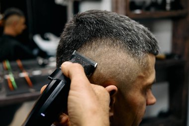 Bir berber, modaya uygun bir berber dükkanındaki müşterisine temiz ve modern bir saç kesimi yapmak için makas kullanır. Aynalar şık ortamın atmosferini yansıtır..