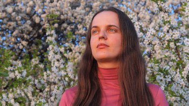 Genç kadın canlı bahar çiçeklerinin arasında duruyor, polen alerjisi ile uğraşırken doğanın güzelliğini deneyimliyor..