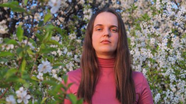 Bir kadın, canlı bir bahar günü, mevsimsel alerjilerden etkilenen narin beyaz çiçeklerle çevrili olarak ayakta durur..