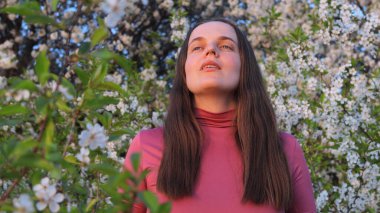 Bahar çiçekleriyle dolu canlı bir bahçede, bir kadın polen alerjileriyle uğraşırken atmosferi büyüler ve nefes almak için zaman ayırır..