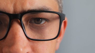 Detaylı bir yakın çekim siyah çerçeveli gözlüklerin arkasındaki kişinin gözüne odaklanır. Lensteki ve etrafındaki deri dokusundaki yansıma açıkça görülebilir, odaklanmayı ve gözlemlemeyi iletir..