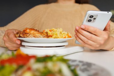 Dijital ölçekte tavuk ve pirinçten oluşan bir öğünü akıllı telefon tutarken ölçmek, muhtemelen diyet ve sağlık için kalori veya makroyu takip etmek.