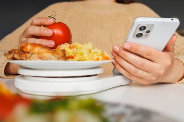 Bir insan, akıllı telefon kullanarak, teknolojiyi, sağlıklı beslenmeyi ve diyet takibini birleştirirken, bir öğün domatesi bir öğün üzerinde tutar..
