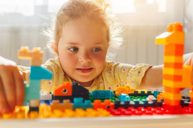 Genç kız rengarenk oyuncak inşaatçıları olan bir bina inşa etmeye odaklanmış, elleri parlak güneş ışığı yaratmakla meşgul. Çocukluk oyunu ve yaratıcılık.