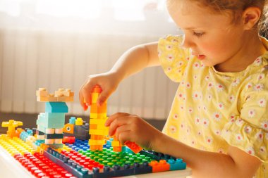 Çocuğun elleri, yaratıcı ve odaklanmış oyunu gösteren canlı oyuncak yapıcı bloklarla bir kale levhasında bina yapmakla meşgul. Çocukluk gelişimi.