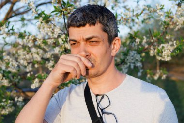 Çiçek açan ağaçların yanında burnunu kapayan adam polene veya kötü kokuya tepki veriyor. Alerji sezonu ya da tatsız koku..