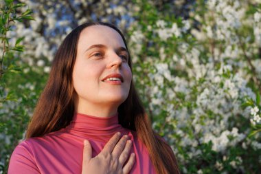 Kadın, açık havada, beyaz çiçeklerin arasında rahatça nefes alır. Alerjisi olmayan, temiz bahar havasının ve doğanın tadını çıkaran bir kadın..