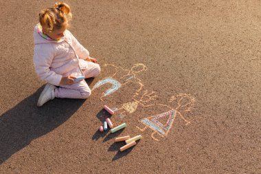 Genç kız asfaltta diz çöküp ailesini renkli tebeşirle çiziyor. Yaratıcı çocukluk sanatı ve açık havada sevdiklerini temsil etmek..