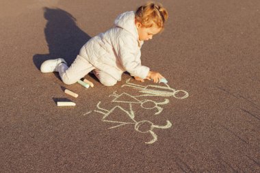 Genç kız diz çöküp kaldırıma beyaz tebeşir çizerek çocukluk yaratıcılığı, açık hava eğlencesi ve geçici sokak sanatı sergileyen bir aile çiziyor..