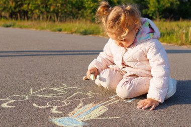 Genç kız kaldırıma tebeşirle çizimler çiziyor, çocukluk yaratıcılığı, açık hava eğlencesi ve geçici sokak sanatı sergiliyor..