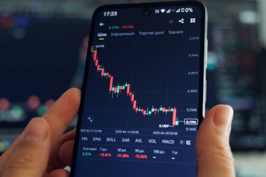 Düşük ışık ayarlı bir ortamda piyasa grafikleriyle çevriliyken akıllı bir telefonla kripto para birimi hareketlerini inceleyen kişi.