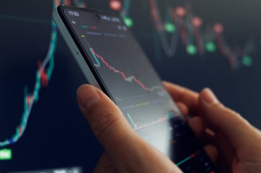Tüccar, ticaret saatlerinde değişen borsa grafikleri ve veri eğilimlerini incelemek için akıllı telefonu kullanır.