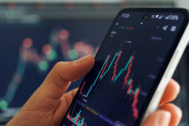 Borsa verilerini rengarenk grafiklerle gösterilen akıllı telefonlarda analiz eden bir kişi, finansal ticaret geçmişi ile karşılaştırır..