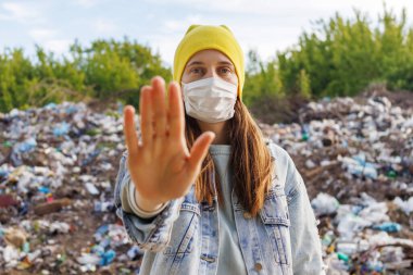 Sarı şapkalı ve maskeli genç bir kadın elini çöp sahasının önünde tutar ve kirliliği durdurması için bir mesaj iletir..