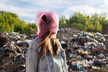 Kafasında pembe plastik poşet olan bir kadın, plastik kirliliğinin tehlikesini ve çevresel etkilerini simgeleyen bir çöp sahasında duruyor..
