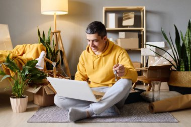 Bir adam yeni evine taşındıktan sonra elinde anahtarlarla kutuları taşırken yerde oturuyor..