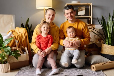 Dört kişilik mutlu bir aile kutuları ve bitkilerle dolu bir odada birlikte gülümsüyor..