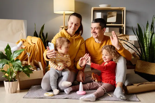 Dört kişilik bir aile, kutuların ve ev eşyalarının arasında oturmuş gülümsüyor ve iletişim kuruyor..