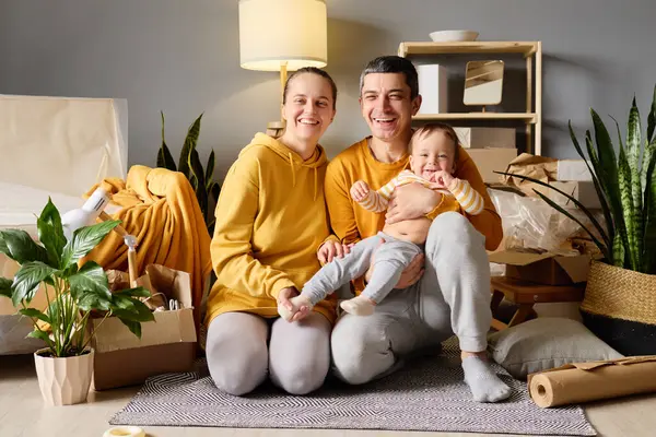 Bebekli mutlu bir aile, yeni evlerindeki paketsiz kutuların arasında kameraya gülümsüyor..