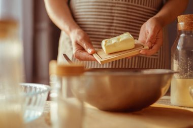 Önlük takan bir insan tereyağını küçük bir tahta üzerinde karıştırma kabının üzerinde tutar..
