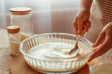 Çizgili önlüklü bir aşçı hamur hamurunu kaşıkla yuvarlak bir cam kabın içine yayar..