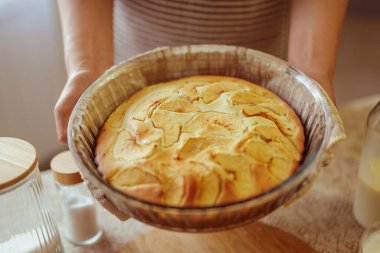 Çizgili önlük giyen bir aşçının elleri, cam bir tabakta taze pişmiş elmalı turta sunar..