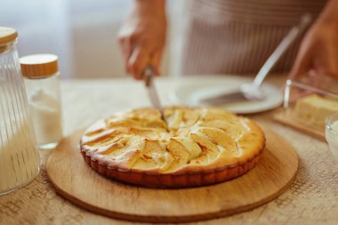 Çizgili önlüklü bir aşçı yeni pişmiş bir elmalı turtayı ahşap bir tahtada kesiyor..