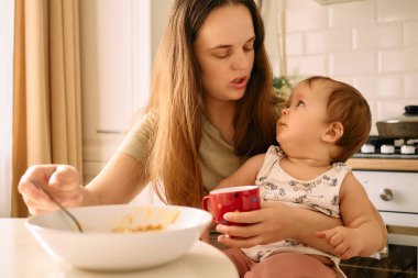 Bir kadın kucağında tuttuğu bir bebekle samimi bir konuşma yapar. İkisi de kısmen yenmiş bir besinle mutfak masasının karşısında birbirlerine dikkatle bakar..