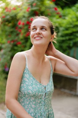 Neşeli genç bir kadın, güneşli bir öğleden sonra çiçeklerin arasında durarak gülümsüyor, pozitiflik ve sıcaklık saçıyor.