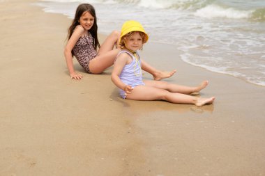 Su kenarında kumlu bir sahilde mayo giymiş iki mutlu genç kız yaz gününün tadını çıkarıyorlar..