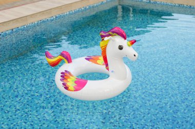 Canlı, şişme bir tek boynuzlu at, parlak mavi bir yüzme havuzunda yüzüyor. Yaz eğlencesi için mükemmel..