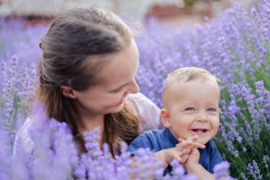 Neşeli bir anne gülümseyen bebeğine sevgiyle bakar. Parlak mavi gözleri ve sarı saçları vardır. Mor lavanta çiçeklerinden oluşan canlı bir tarlada birlikte otururlar..