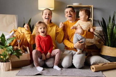 Dört çocuklu neşeli aile başarılı bir hareketi kutluyorlar. Yeni evlerinde yumruklarını havaya kaldırıyorlar. Kutularla çevrili..