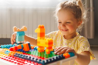 Neşeli küçük bir kız renkli yapı taşlarıyla oynayıp sarı bir zürafa yaratıyor. Odaklanmış ve mutlu, yüzünde parlak bir güneş ışığı var..
