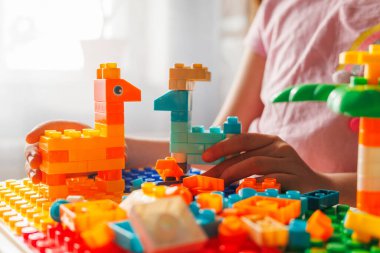 Küçük bir kızın elleri renkli yapı taşlarıyla bir çift zürafa yaratmakla meşgul. Parlak güneş yaratıcı oyun üzerinde parlıyor, çocukluğun eğlence ve hayal gücünü vurguluyor..