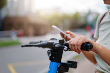 Şehir caddesinde elektrikli scooter 'ı açmak ya da kullanmak için akıllı telefon kullanan bir insanın yakın çekimi, kentsel hareketlilik ve teknolojiyi gösteriyor.