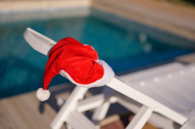 Bir Noel şapkası, yüzme havuzunun yanındaki beyaz bir şezlongun arkasında duruyor..