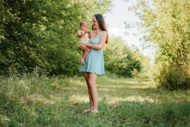 Güneşli bir açık havada bebeğini kucağında tutan mutlu bir anne..