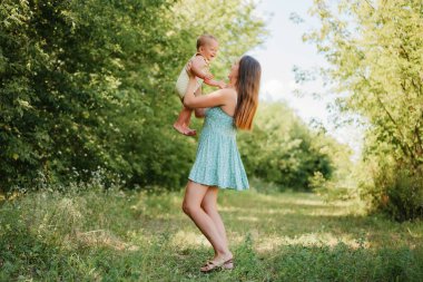 Güneşli bir açık havada bebeğini kucağına alıp kaldıran mutlu bir anne..