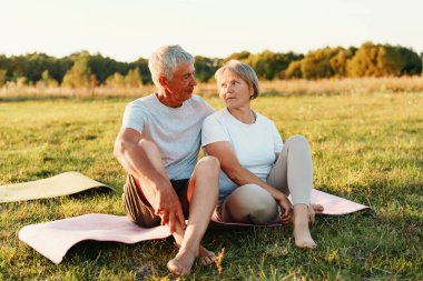 Olgun çift yoga minderlerinde oturuyor ve gün batımında çimenli bir tarlada birbirlerine bakıyor..